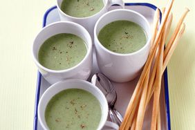 multiple mugs of creamy broccoli soup on a white tray