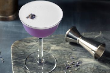 lavender cocktail with measuring jigger on a marble cutting board