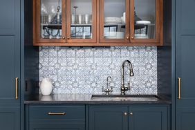 A kitchen sink with a beautiful pattern tiled backsplash with a chrome faucet, black granite countertops, and surrounded by blue and wood cabinets.