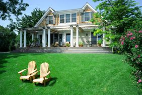 Two wood chairs on a beautiful green, lush lawn with large house in the background