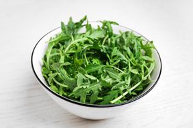 Fresh arugula in bowl on white wooden table