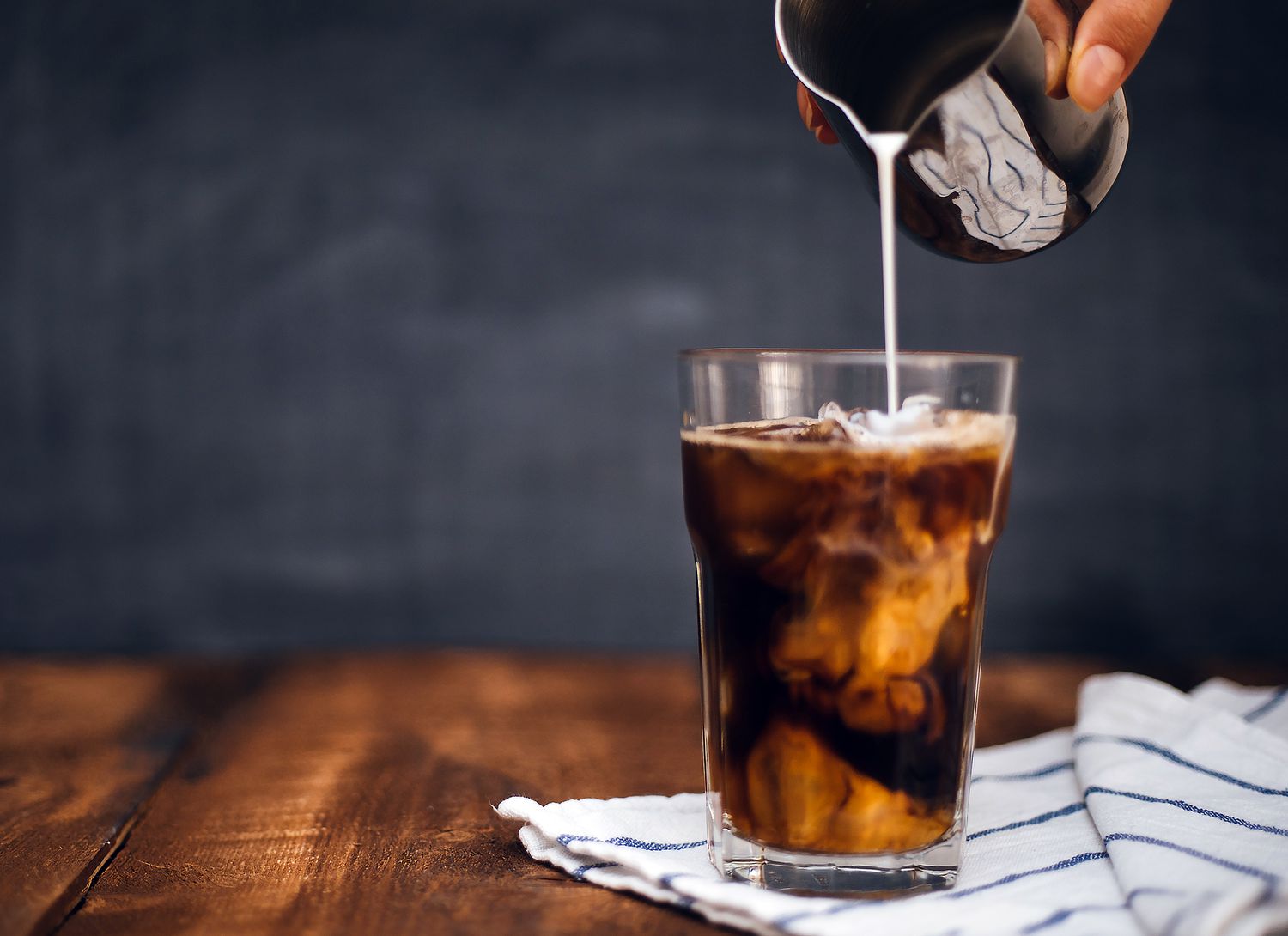 glass of iced coffee with milk being poured into it