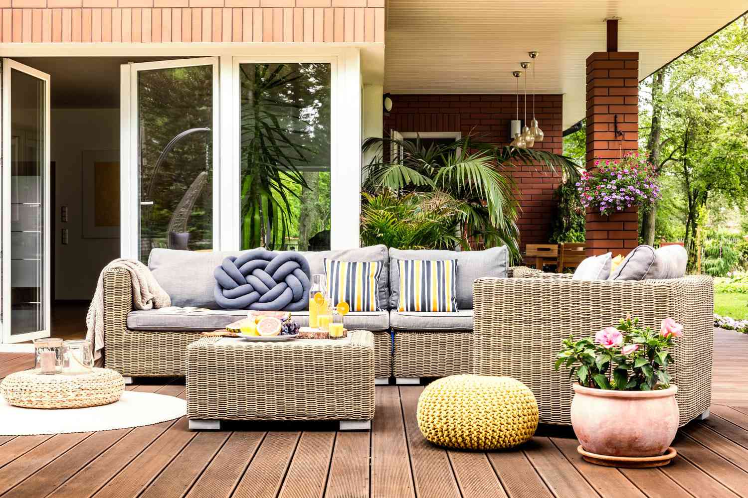 Beige garden furniture with striped pillows on wooden terrace with pink flowers and poufs