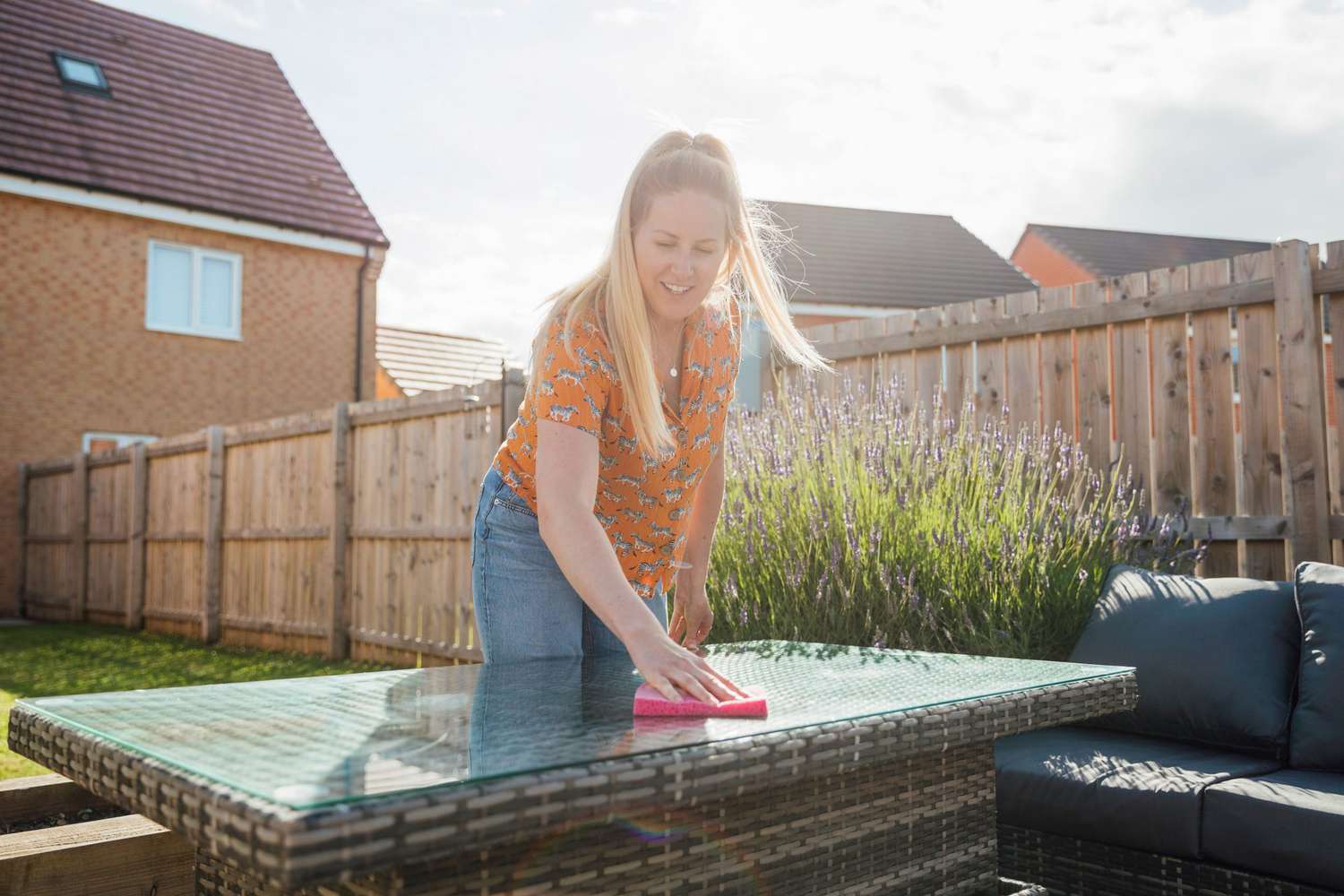 Woman smiling, leaning over to clean a table outdoors in summer