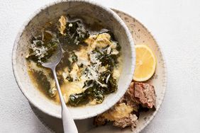 stracciatella soup with kale and lemon served in grey bowl with bread and lemon on the side