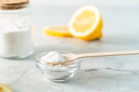 Jar with baking soda, lemon and wooden spoon on marble table background.